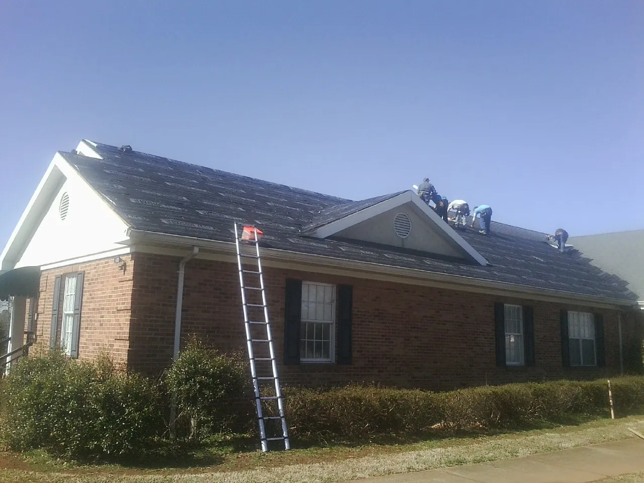 Crew tearing shingles off a brick ranch roof with a ladder set — Emergency Roof Repair work by our crew in Monmouth Junction
