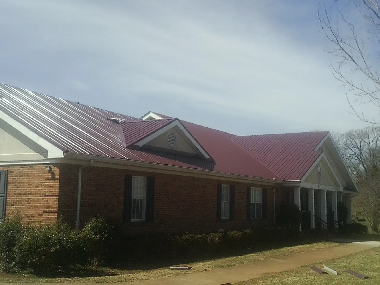 Red metal roof with gabled entries on a long brick building, from a Hail Damage Roof Repair job in Monmouth Junction