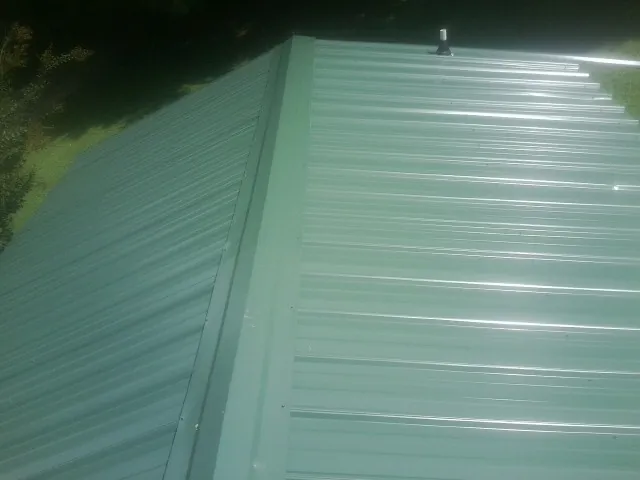 New green metal panels meeting at the ridge of a roof — Flat Roof Repair work by our crew in Monmouth Junction
