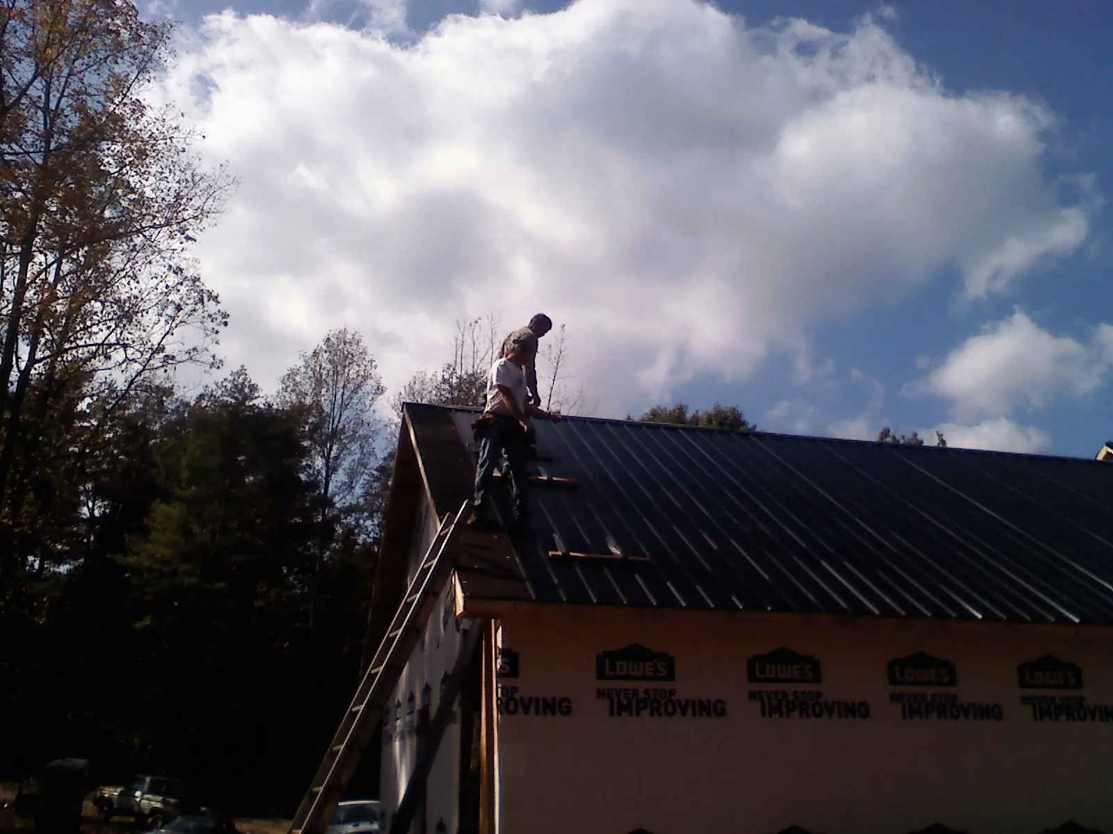 Roofer fastening dark metal panels high against a cloudy sky, from a Roof Inspection job in Monmouth Junction