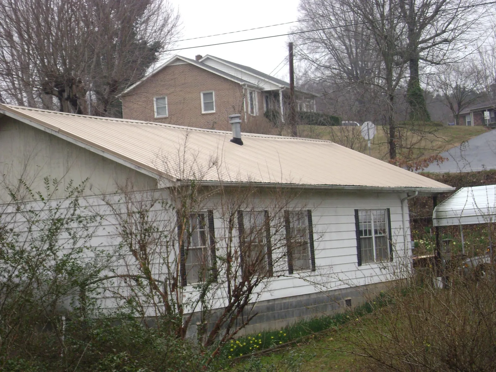 Tan metal roof on a white sided house set into a hillside — Commercial Roofing by Roofing Brothers in Monmouth Junction